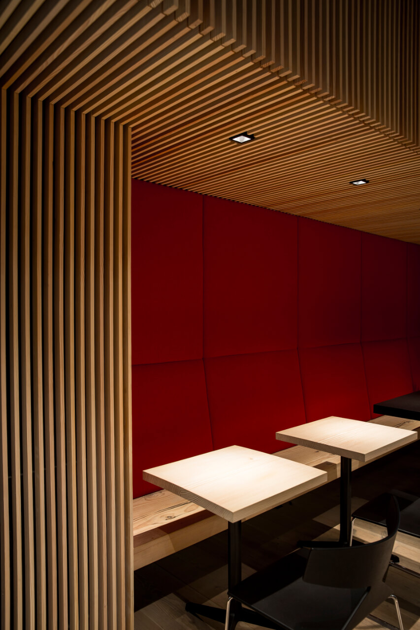 Sushi bar restaurant with small tables and corner bench and light wooden wall and ceiling panelling.