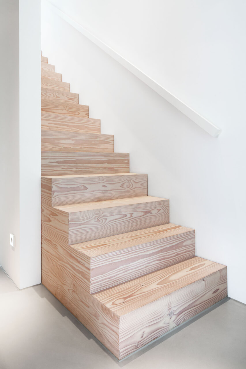 Treppe aus hellem Holz mit weißem Treppenaufgang und hellgrauem Betonboden